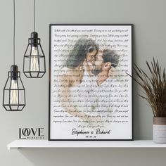 a couple kissing in front of a framed photo on a shelf next to two hanging lights