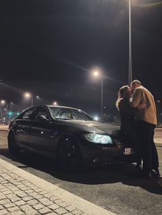 two people standing next to a parked car at night