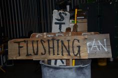 a wooden sign sitting on top of a trash can next to a metal container with writing on it