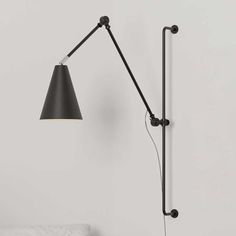 a black lamp on a white wall next to a bed with a pillow and headboard