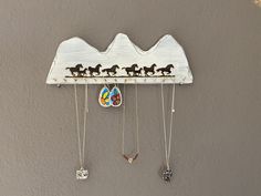 a wooden sign with horses on it hanging from the wall next to two necklaces