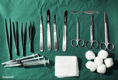 several surgical instruments are laid out on a green tablecloth with cotton swabs