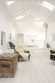 a living room with white walls and wooden flooring, two wicker chairs and an ottoman