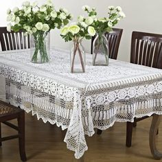 three vases with flowers are sitting on a table in front of two wooden chairs