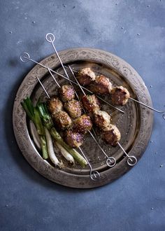 several skewered meats and asparagus on a plate with tongs