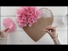 someone is making a paper heart with pink flowers and tissue pom - poms