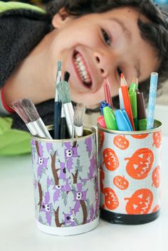 a young boy is smiling next to two cups with toothbrushes and brushes in them