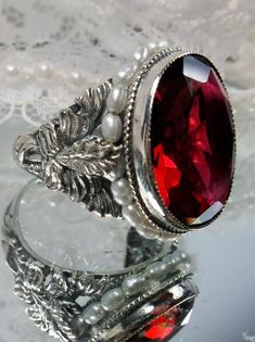 This detailed ring is an antique reproduction beautifully crafted in solid sterling silver. The lovely ring is set with a flawless man-made/simulated red ruby gemstone. The oval gem is 18mm long by 16mm wide. The inside of the band is marked 925 for solid sterling silver. Notice the intricate and detailed palm tree and floral design of the silver filigree setting and band. Tiny seed pearls create a beautiful outline for the gemstone. This is an exquisite rendition of an antique filigree ring. Collectible Silver Garnet Jewelry, Vintage Garnet Ruby Ring With Intricate Design, Antique Sterling Silver Ruby Wedding Ring, Antique Sterling Silver Ruby Ring For Wedding, Vintage Sterling Silver Ruby Ring For Formal Occasion, Antique Red Engraved Ring, Victorian Style Silver Ruby Ring For Anniversary, Victorian Style Silver Ruby Ring For Wedding, Victorian Ruby Jewelry For Collectors