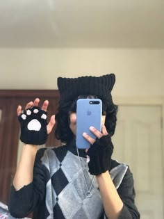 a person wearing a cat hat and mittens holding up a cell phone to their face