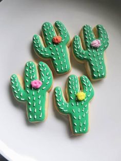 three decorated cactus cookies on a plate with pink and yellow flowers in the top one