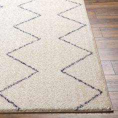 a white rug with black lines on the floor and wooden floors in front of it