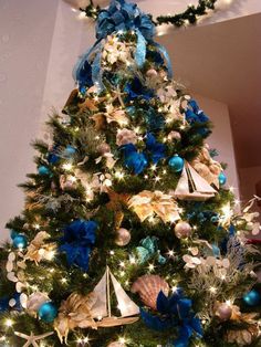 a christmas tree decorated with blue and gold ornaments, bows and seashells is shown