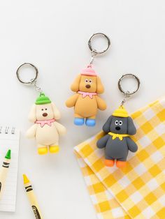 three keychains with cartoon characters on them next to a notepad and pen