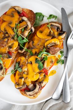 a white plate topped with sliced mushrooms and veggies next to a knife and fork