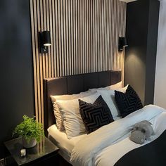 a bed with white sheets and black pillows in a room next to a wall mounted lamp