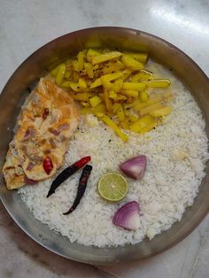 a pan filled with rice, meat and vegetables on top of a table next to lemon wedges