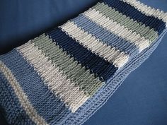 a crocheted blanket laying on top of a blue bed cover with white and gray stripes