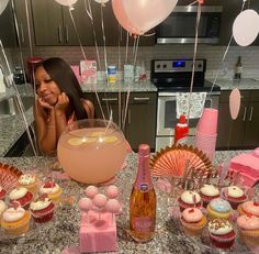 a woman sitting at a table with cupcakes, champagne and other desserts