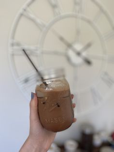 a person holding a mason jar in front of a clock