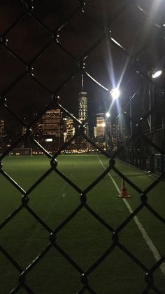 an empty soccer field at night with the lights on and buildings in the back ground