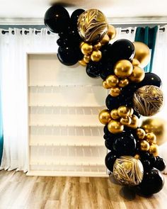 black and gold balloons are hanging from the ceiling in front of a white bookcase