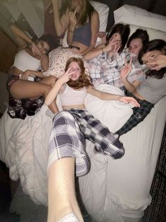 a group of young women laying on top of a bed next to each other with their hands in the air