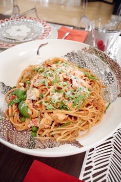 a white plate topped with pasta covered in sauce and vegetables next to silverware on a wooden table