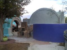 an outdoor kitchen area with blue walls and stone ovens in the background, surrounded by trees