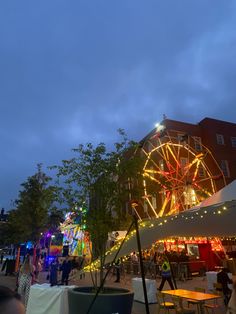 an amusement park at night with lights on the ferris wheel and people walking around it