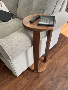 a remote control sitting on top of a wooden table next to a couch with a book on it