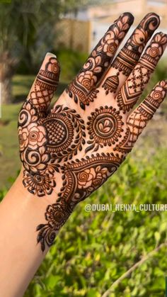 a hand with henna on it and green plants in the backgroung