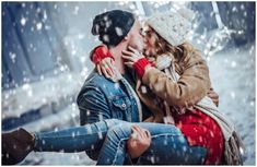 a man and woman kissing in the snow with falling snowflakes behind them on a cold winter day