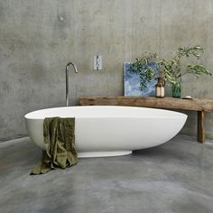 a large white bath tub sitting on top of a cement floor next to a wooden table