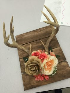 a deer's antlers with flowers and leaves on them sitting on top of a piece of wood