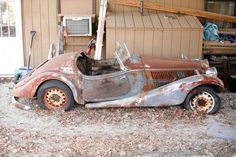 an old rusted out car is parked in front of a building with junk on the ground