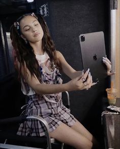 a woman sitting in a chair with her eyes closed and holding a cell phone next to an apple computer