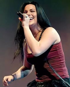 a woman with long black hair holding a microphone in her right hand and singing on stage