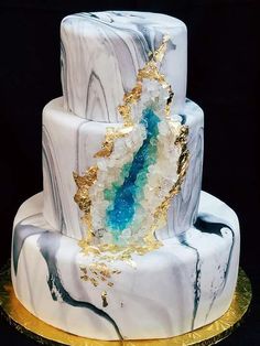 a three tiered white and blue cake with gold accents