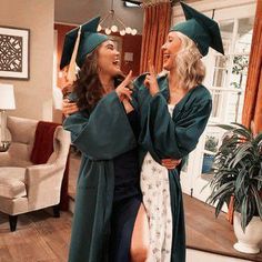 two women dressed in graduation gowns and hats are laughing while one holds her hand on the other's shoulder