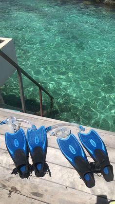 three pairs of blue and black diving equipment sitting on a wooden dock next to clear water