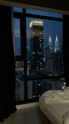 a bedroom with a large window overlooking the city at night, and there is a bed that has white sheets on it