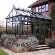 a green glass house sitting on top of a lush green field next to a brick building