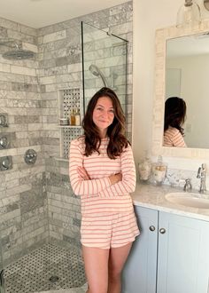 a woman standing in front of a bathroom mirror next to a sink and shower stall