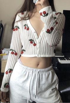 a woman wearing white shorts and a crop top with cherries on it, holding a cell phone up to her face