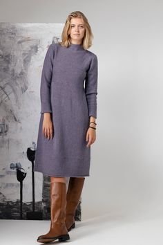 a woman standing in front of a painting wearing boots and a purple dress with long sleeves