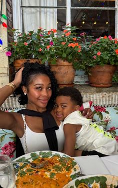 a woman sitting next to a child at a table with plates of food on it