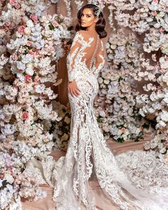 a woman in a white wedding dress standing next to a floral wall with flowers on it