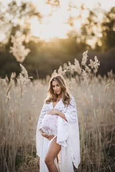 a pregnant woman poses in a field with her belly wrapped around her waist and wearing a white dress