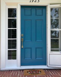 Silken Peacock blue teal front door; Ikea Christmas floral welcome mat with red, white, green, teal, pink, and black; white sidelights; brick front porch Silken Peacock Sherwin Williams Front Door, Teal Blue Front Door, Dark Teal Front Door, Peacock Paint Colors, Silken Peacock, Teal Front Door, Brick Front Porch, Paint Pallette