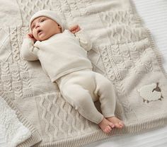 a baby laying on top of a blanket next to a white blanket with a knitted hat